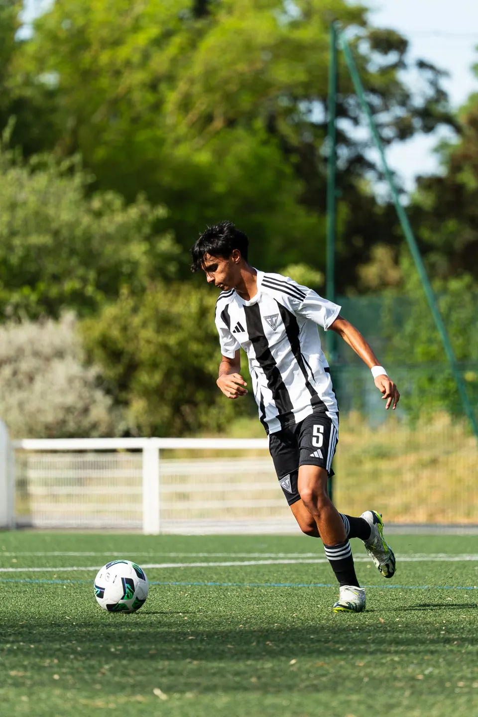 Young player in a black and white striped shirt dribbling the ball
